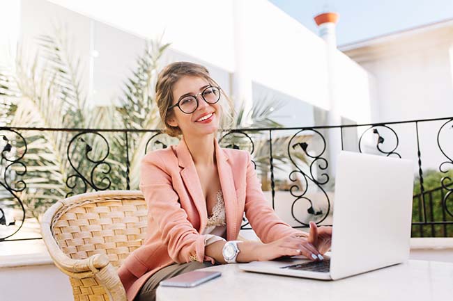 Young woman sitting in wicker chair and working on a laptop - ZenQ Designs